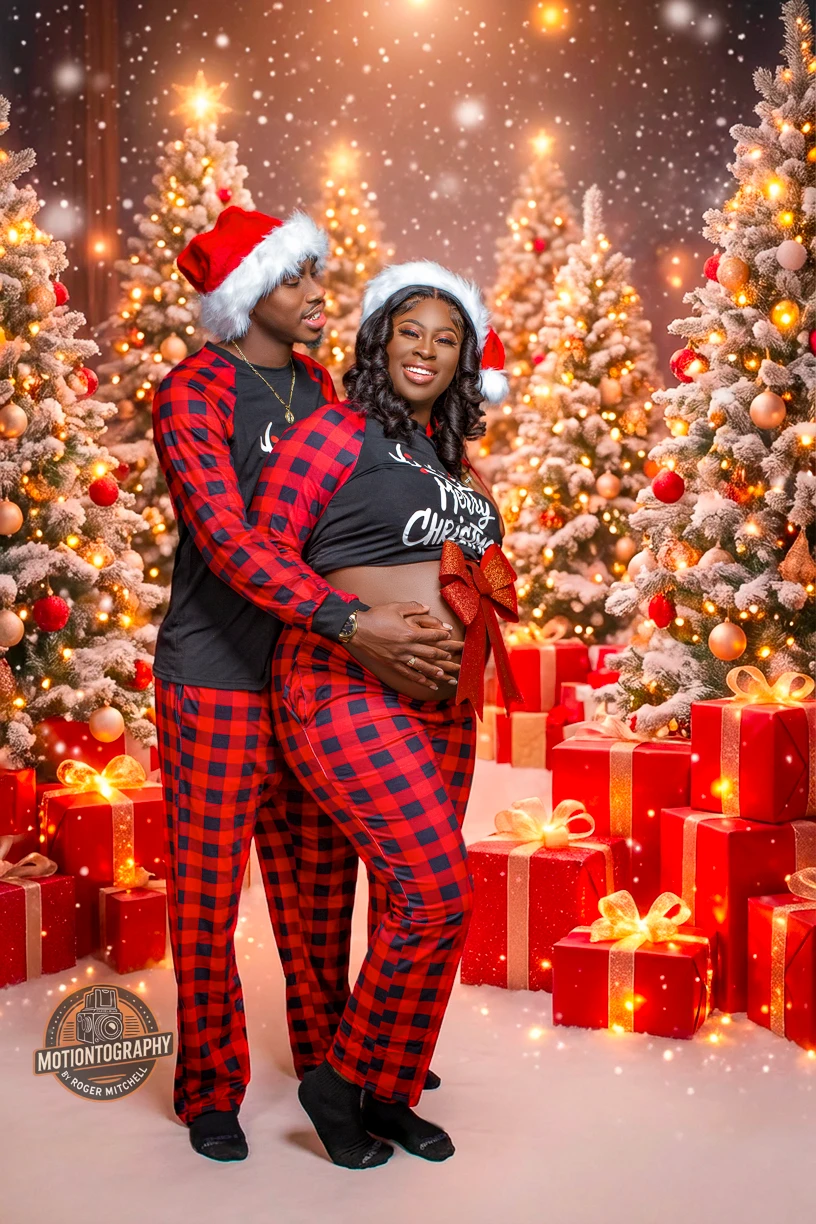 Expecting couple wearing matching red plaid Christmas pajamas pose in a festive scene with Christmas trees, holiday lights, and gift boxes in Hampton Roads, Virginia.