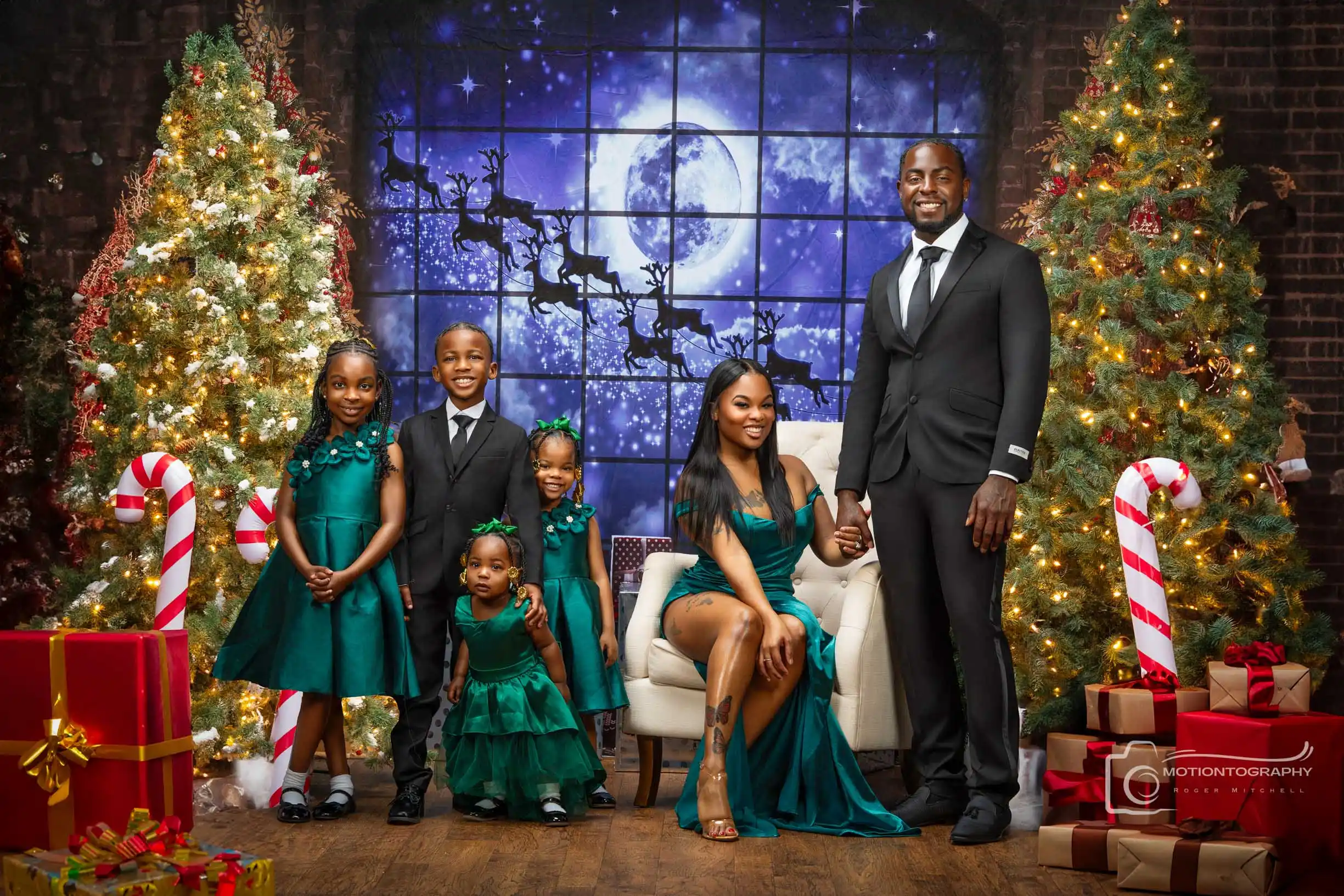 Formal family Christmas portrait featuring mother and daughters in emerald green gowns and father and son in black suits, set against a magical holiday backdrop.
