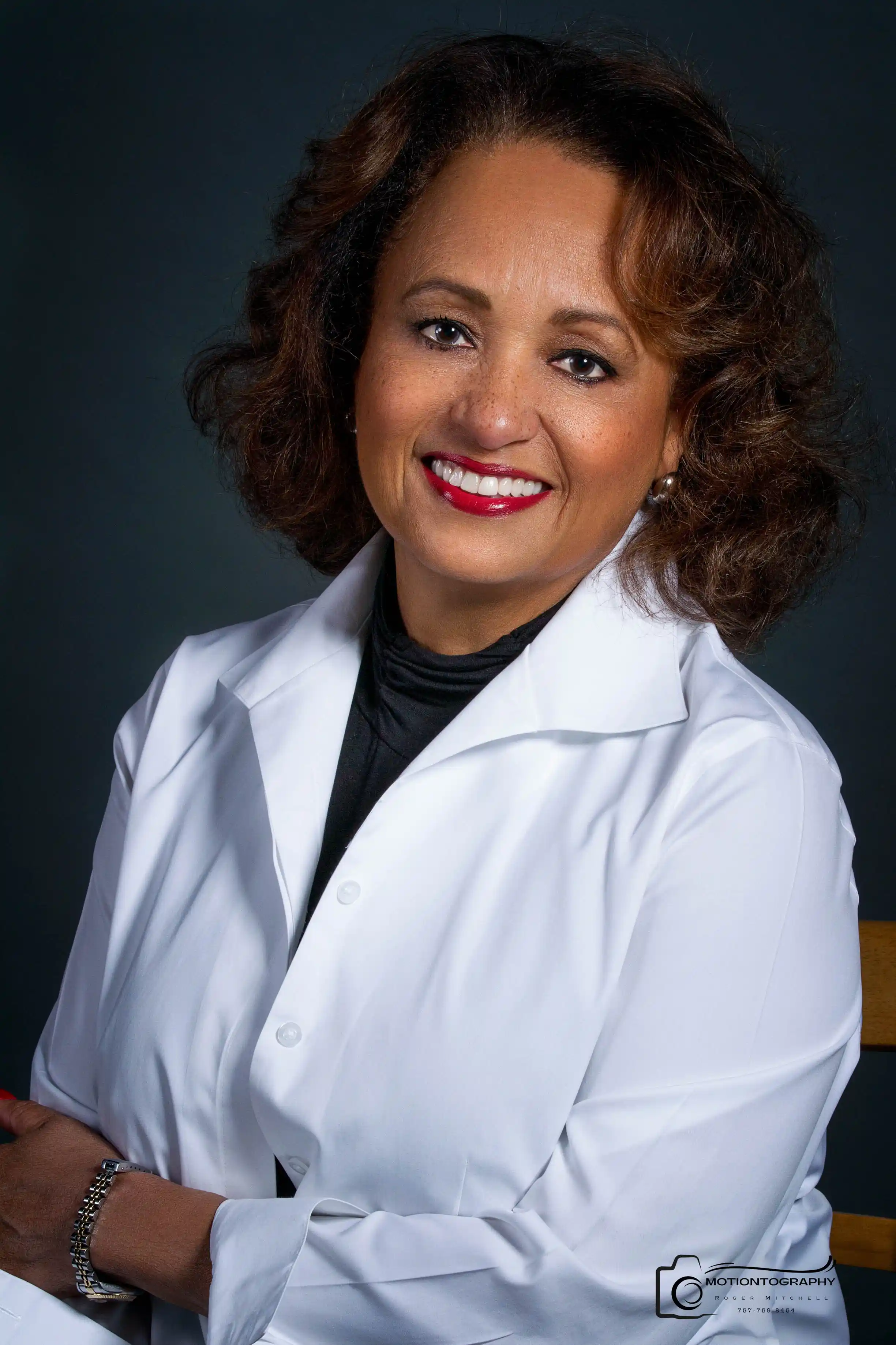 Daphne Reid smiling in a white coat against a dark background