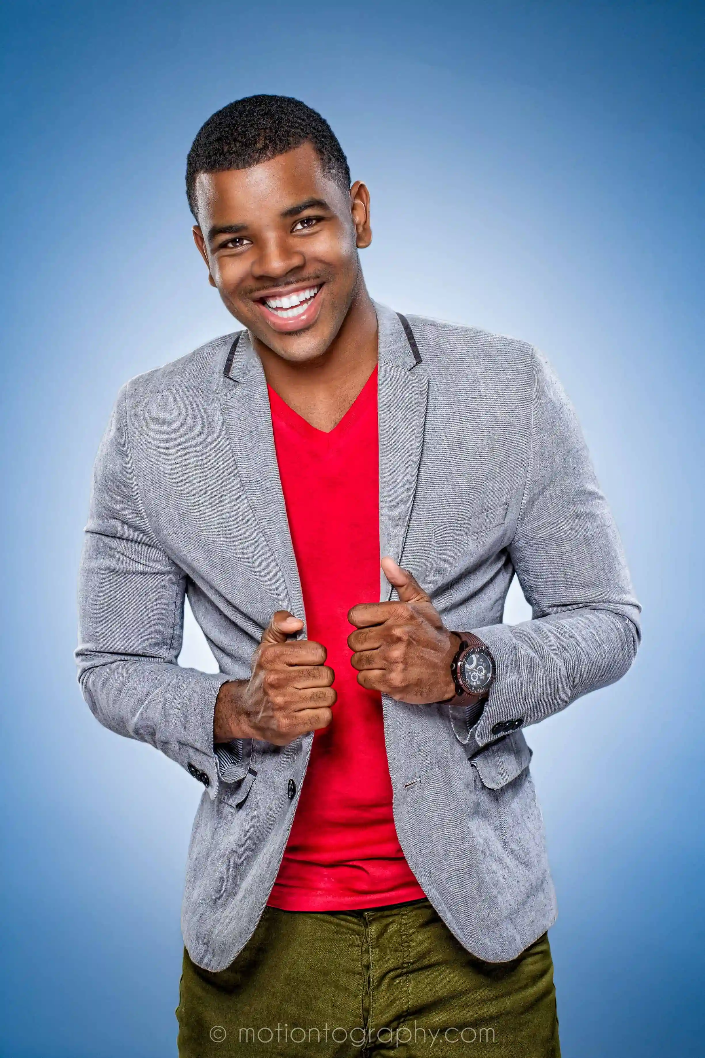 Jermelle Simon wearing a red shirt and grey blazer, smiling and posing against a blue background.