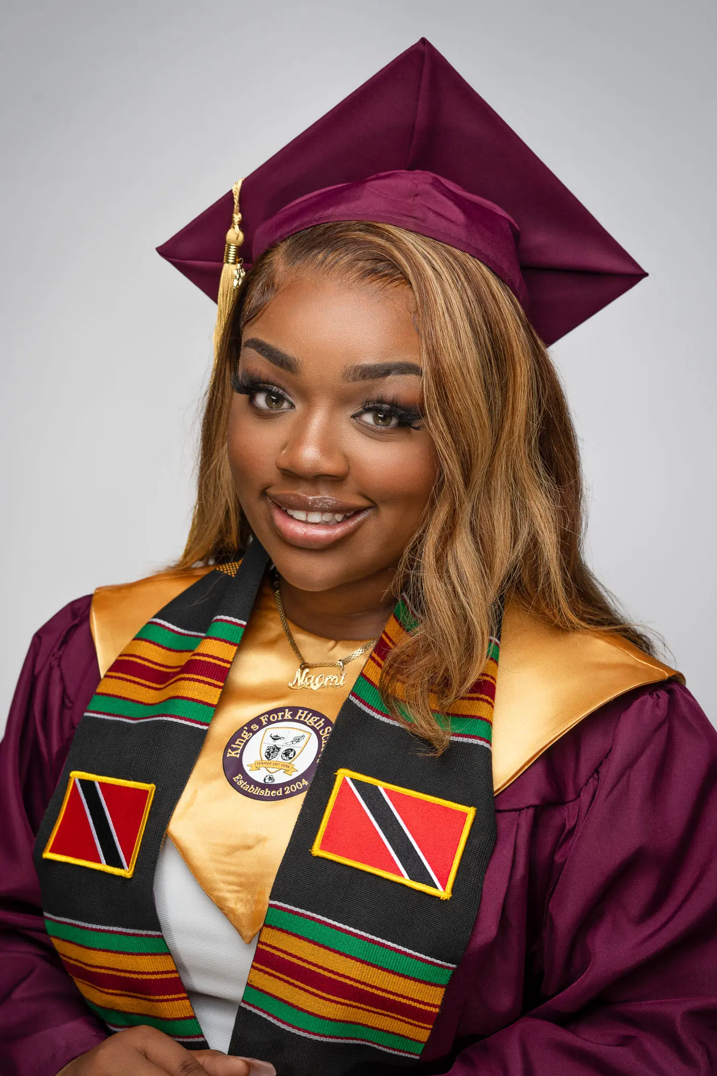 King's Fork High School graduation portrait featuring a student wearing a maroon cap and gown with a Trinidad and Tobago flag stole.