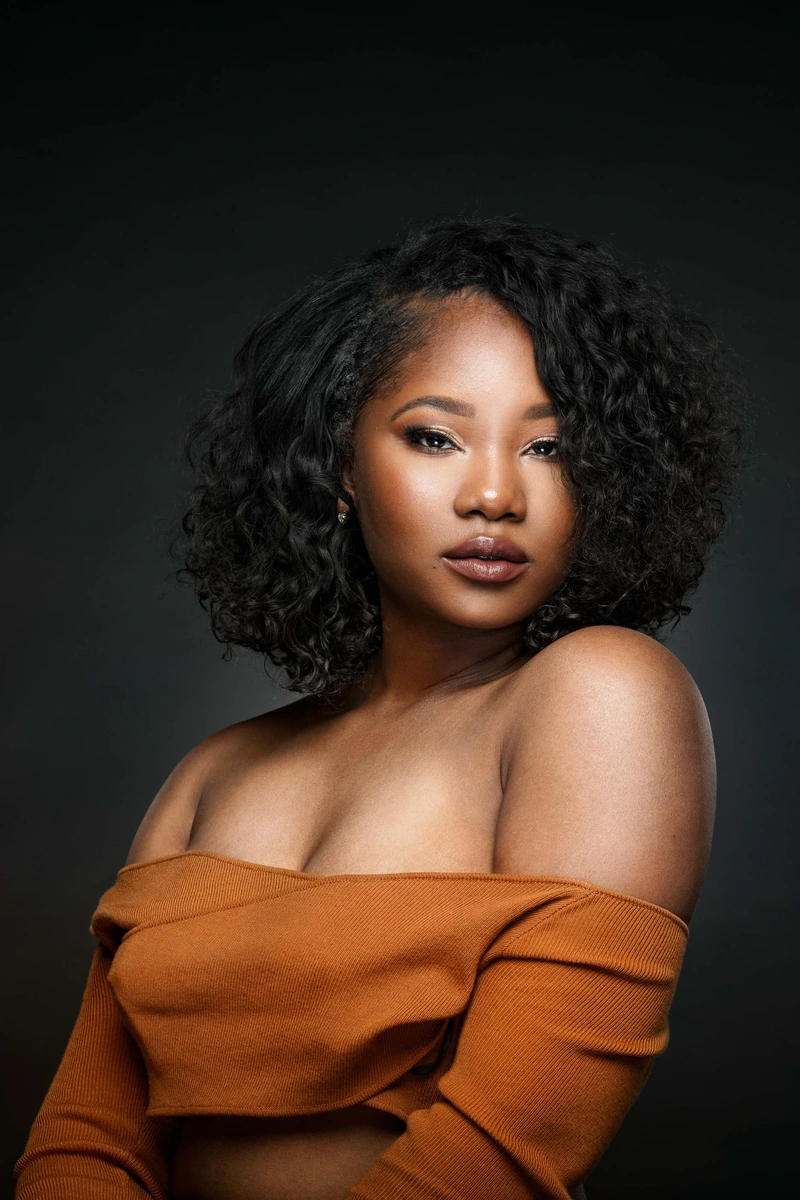 Studio portrait with curly hair and orange off-shoulder top by Motiontography